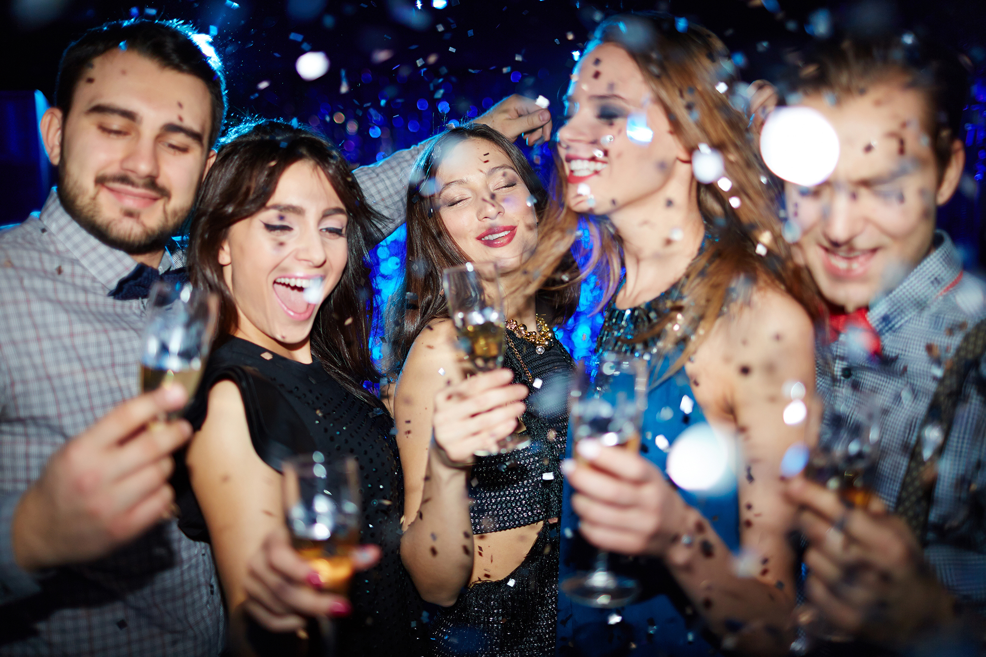 Group of ecstatic friends cheering with champagne at party in night club